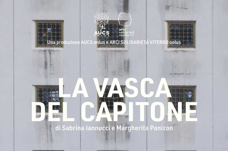 Parte della locandina del documentario, l’intera immagine è occupata dal muro della Casa Circondariale grigio chiaro con sei finestre quadrate munite di sbarre.