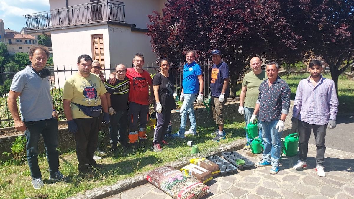 Il gruppo di partecipanti al progetto all'esterno durante una pausa. Al centro dell'immagine dei sacchi di terriccio e dei vasi, sulla destra le persone hanno in mano degli innaffiatoi